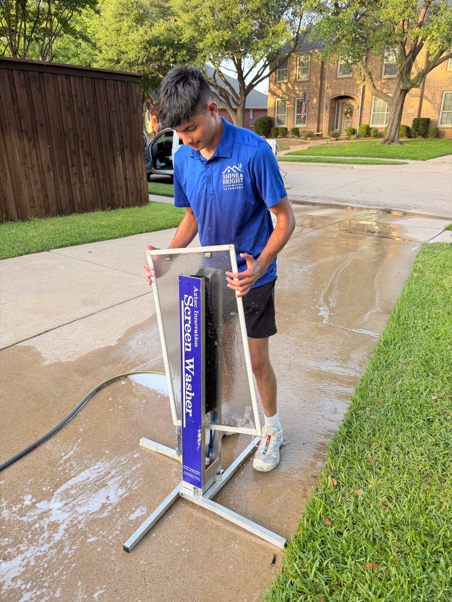 Shine & Bright technician washing a window screen on a screen-washing stand in a driveway